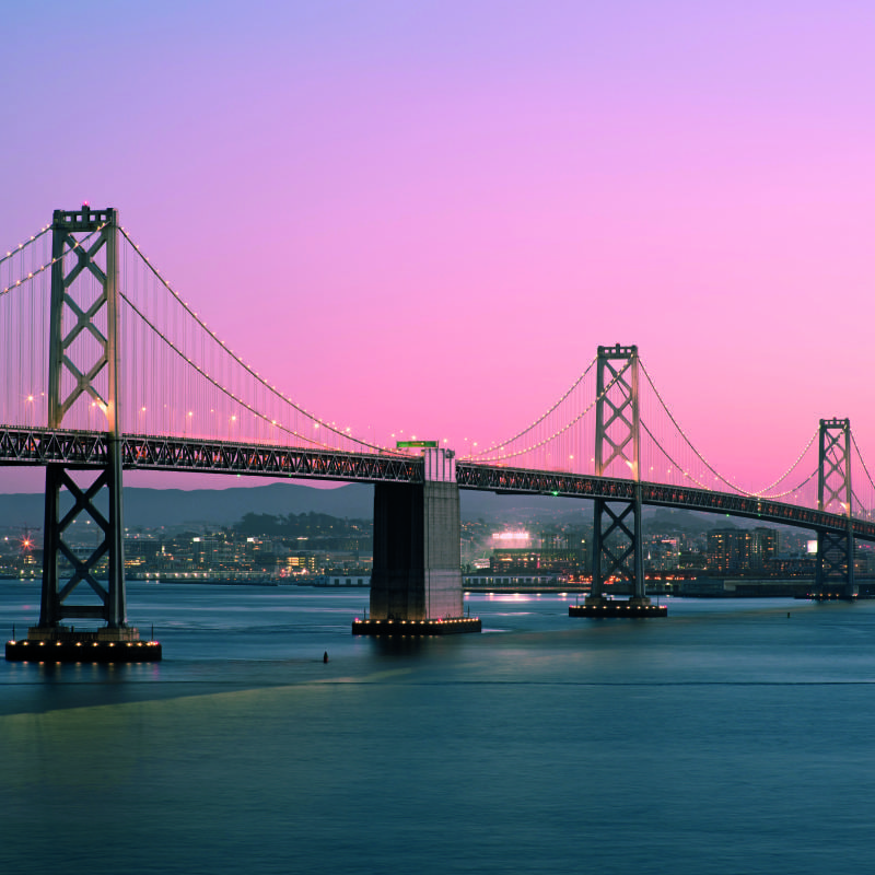 San Francisco Bay Bridge wall mural at sunset in a living room with a grey chair