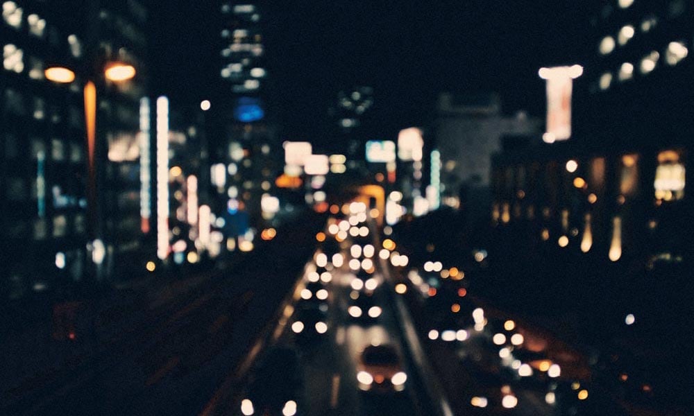 Out of focus night-time cityscape with illuminated buildings and cars