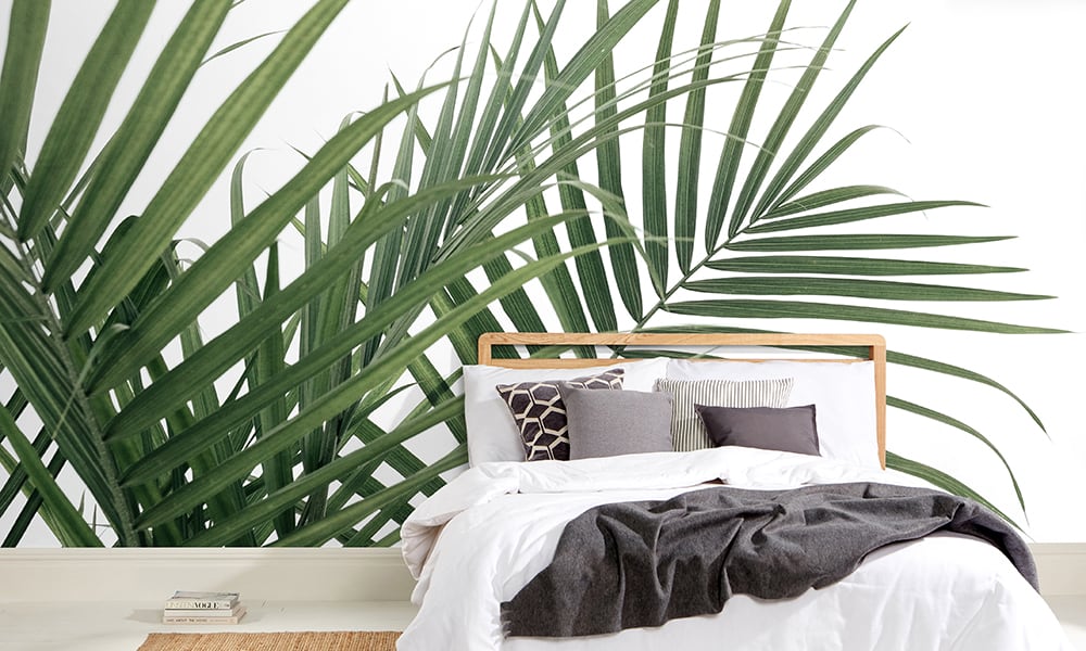 Green palm leaf wall mural with white background in a scandi style bedroom 