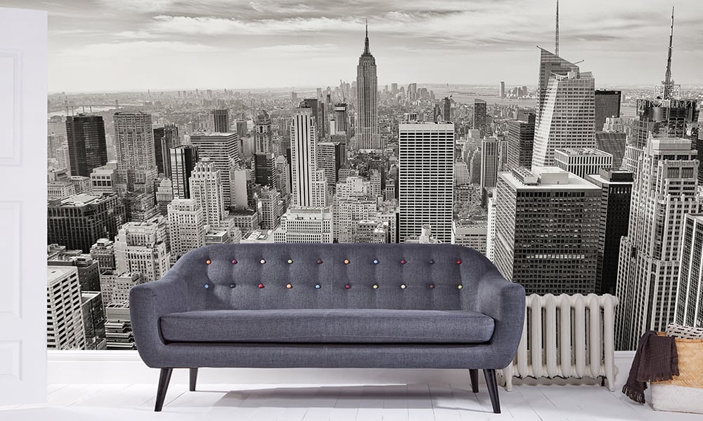 Black and white wallpaper of New York skyline in a living room with grey sofa