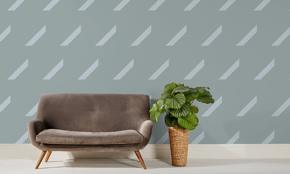 Large scale blue repeat pattern wallpaper with grey sofa and plant