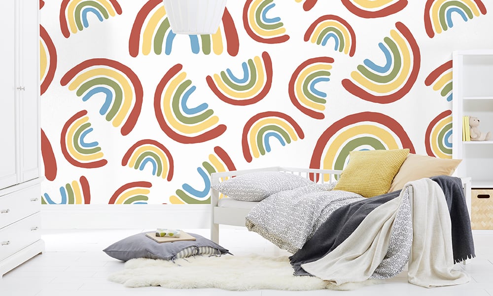 Large scale rainbow wallpaper design situated in kids bedroom in white colourway