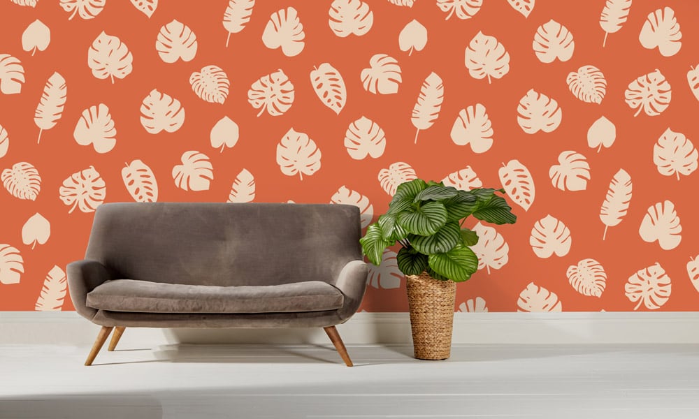 Large scale wallpaper leaves orange background with sofa and cheese plant